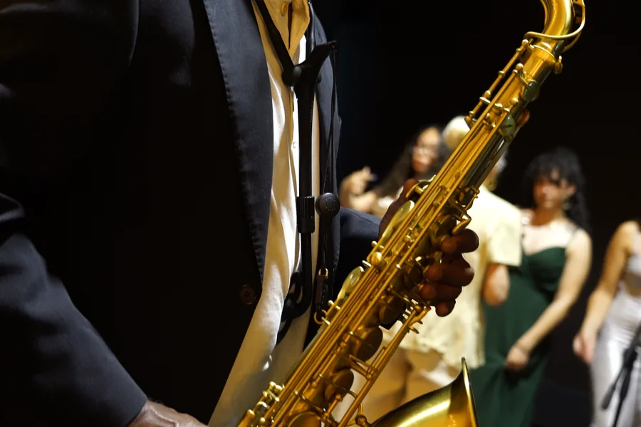 Primer plano del saxo tenor en el escenario, con las coristas desenfocadas al fondo.